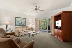 Ein Wohnzimmer mit einer Couch, Sesseln, einem Couchtisch, einem Fernseher und einem Deckenventilator.