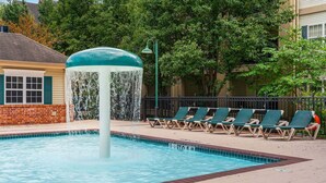A swimming pool with a water feature, surrounded by lounge chairs and a brick wall. - Branson 2BR Condo | Pool • Hot Tub • Balcony (Branson)