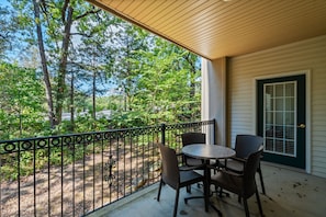 A covered patio with a table and chairs, a view of trees, and a door with a window. - Branson 2BR Condo | Pool • Hot Tub • Balcony (Branson)