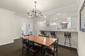 A dining area with a wooden table and chairs, a chandelier, and a kitchen in the background. - Branson 2BR Condo | Pool • Hot Tub • Balcony (Branson)