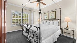Uma cama com dossel e cortina, um criado-mudo com abajur, e quadros nas paredes.