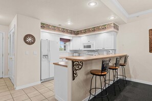 A kitchen with white cabinets, a central island with stools, a microwave, and a refrigerator. - Family-Friendly 2BR Near Silver Dollar City (Branson)