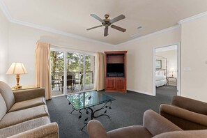 Ein Hotelzimmer mit einem Glastisch, zwei Sofas, einem Fernseher und einem Deckenventilator.