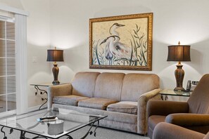A living room with a sofa, armchair, glass coffee table, lamps, and a framed painting on the wall. - Branson Condo | 2 King Suites | Great Location (Branson)