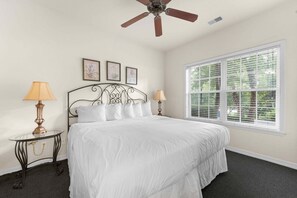 Ein Schlafzimmer mit einem Bett, zwei Nachttischlampen, einem Deckenventilator, einem Fenster mit Jalousien und drei gerahmten Bildern an der Wand.