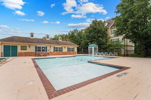 Piscina com uma fonte, um pátio de tijolos e um edifício com uma porta verde.