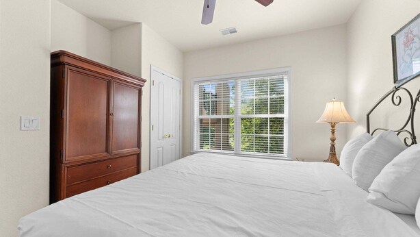 A bedroom with a large bed, a wardrobe, a window with blinds, a ceiling fan, and a bedside lamp. - French Quarter Resort | Close to Shows & Shopping (Branson)
