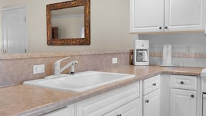 A kitchen with a double sink, a coffee maker, and white cabinets. - French Quarter Resort | Close to Shows & Shopping (Branson)
