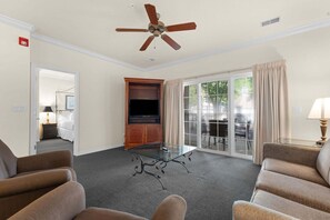 A hotel room with a ceiling fan, a television on a wooden cabinet, a glass coffee table, and a seating area with sofas. - French Quarter Resort | Close to Shows & Shopping (Branson)