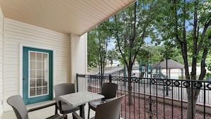 A balcony with a table and chairs, a door with a window, and a view of a playground and trees. - French Quarter Resort | Close to Shows & Shopping (Branson)