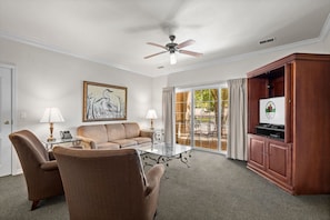 A living room with a sofa, two armchairs, a glass coffee table, a ceiling fan, a painting, and a television on a wooden cabinet. - Branson Family Getaway | 2BR Resort Condo | Pool (Branson)