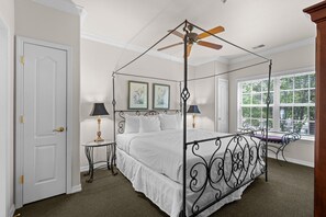 Ein Bett mit Baldachin, ein Deckenventilator, zwei Nachttische mit Lampen und ein Fenster mit Jalousien.