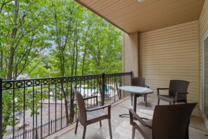 Ein Balkon mit Tisch und Stühlen, Blick auf Bäume und einem Metallgeländer.