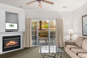 A living room with a fireplace, a television, a sofa, a coffee table, and a view of a garden through glass doors. - Prime Branson Getaway | Near the Strip & Shows (Branson)