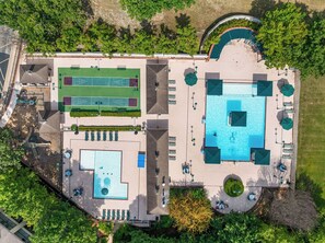Eine Luftaufnahme eines Resorts mit einem großen Schwimmbad, Tennisplätzen und Außenbereich-Sitzgelegenheiten.