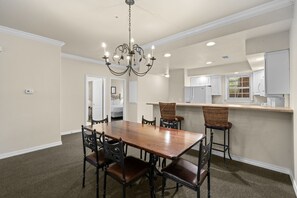 A dining area with a wooden table and chairs, a chandelier, and a kitchen in the background. - French Quarter Resort | The Perfect Branson Location (Branson)