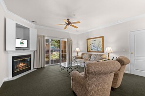 A living room with a fireplace, a ceiling fan, a sofa, a coffee table, and a painting on the wall. - Stay in the Heart of Branson | French Quarter (Branson)