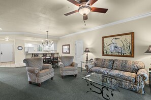 A living room with a ceiling fan, a dining area with a chandelier, and a painting of birds on the wall. - Branson Strip Condo | Pool • Hot Tub • 2 Kings (Branson)