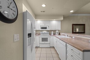 Una cucina moderna con mobili bianchi, forno integrato, microonde e frigorifero.