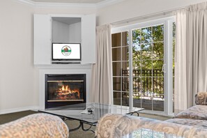 A living room with a fireplace, a television mounted above it, and a large sliding glass door leading to an outdoor area. - Near Highway 76 | Spacious 2BR Resort Condo (Branson)