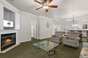A living room with a fireplace, two patterned armchairs, a glass coffee table, and a ceiling fan. - Pet Friendly Condo | Prime Branson Location (Branson)