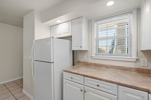 Una cucina con mobili bianchi, un frigorifero bianco, una finestra con persiane e un piano di lavoro color beige.