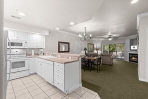 A modern kitchen with white cabinetry, a central island, and a dining area with a fireplace. - Pet Friendly Condo | Prime Branson Location (Branson)