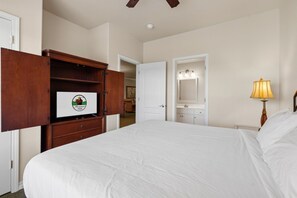 A hotel room with a large bed, a wooden wardrobe, a bathroom with a mirror and lights, and a ceiling fan. - Pet Friendly Condo | Prime Branson Location (Branson)