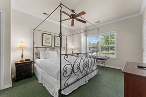Ein Himmelsbett mit Baldachin, ein Deckenventilator, zwei Nachttische mit Lampen und ein Fenster mit Jalousien.