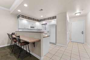 Una cocina con armarios blancos, una isla central y una zona de comedor con taburetes de bar.