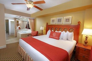 Ein Hotelzimmer mit Bett, Nachttisch, Lampe, Deckenventilator und einem durchgegangene Tür erkennbaren Badezimmer.