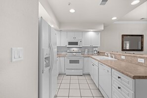 Una cocina moderna con armarios blancos, microondas integrado, horno y lavavajillas, además de una encimera con fregadero.