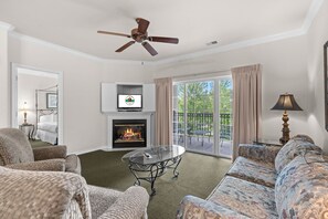 A living room with a fireplace, a ceiling fan, a television, and a view of the outdoors. - Close to Everything Branson | 2 King Bedroom Condo (Branson)