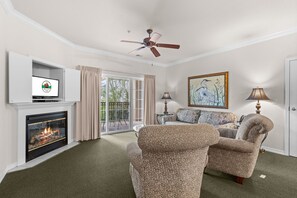 A living room with a fireplace, a ceiling fan, a sofa, and a painting on the wall. - Close to Everything Branson | 2 King Bedroom Condo (Branson)