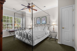Ein Himmelbett mit Deckenventilator, zwei gerahmte Kunstwerke, ein Nachttisch mit Lampe und eine Tür.