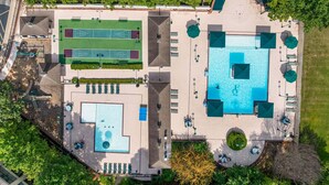 Vista aérea de un complejo turístico con una gran piscina, canchas de tenis y zonas de estar al aire libre.