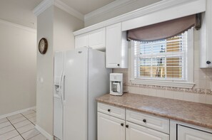 A kitchen with white cabinets, a refrigerator, a coffee maker, and a window with blinds. - Branson Strip Condo | Pool • Hot Tub • 2 Kings (Branson)