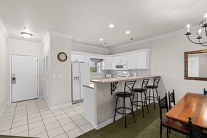 A compact kitchen with white cabinets, a microwave, a toaster, and a sink. There is a dining area with a wooden table and four chairs. - Branson Strip Condo | Pool • Hot Tub • 2 Kings (Branson)