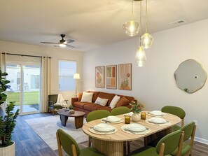A dining area with a round table set for six, surrounded by green upholstered chairs.