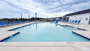 Una piscina amb vores de rajola blava i blanca, envoltada de gandules blaves i un edifici blanc amb un senyal que indica un interruptor d'emergència de la piscina.
