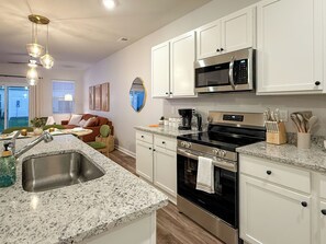 A modern kitchen with white cabinets, stainless steel appliances, and a granite countertop. - Modern 3BR/3BA Family Home - Beach • Pool • Shops (Myrtle Beach)
