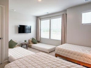A hotel room with three single beds, a flat-screen TV mounted on the wall, and a window with blinds.