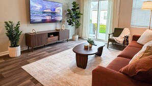 A living room with a flat-screen TV, a sofa, a coffee table, and a potted plant. - Modern 3BR/3BA Family Home - Beach • Pool • Shops (Myrtle Beach)