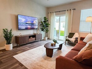 A living room with a flat-screen TV, a sofa, a coffee table, and a potted plant. - Modern 3BR/3BA Family Home - Beach • Pool • Shops (Myrtle Beach)