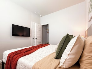 Ein Schlafzimmer mit einem Bett, einem an der Wand montierten Fernseher und einer Tür zu einem Kleiderschrank.