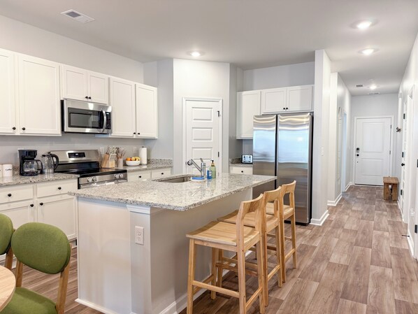 A modern kitchen with white cabinets, stainless steel appliances, a granite countertop, and a bar area with wooden chairs.