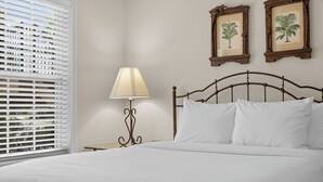 Ein Bett mit weißer Bettwäsche, eine Nachttischlampe und zwei gerahmte Pflanzenbilder an der Wand.
