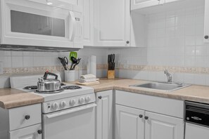 A kitchen with white cabinets, a stove, a microwave, a sink, and various kitchen utensils. - Pet Friendly Queen Condo | French Quarter Resort (Branson)
