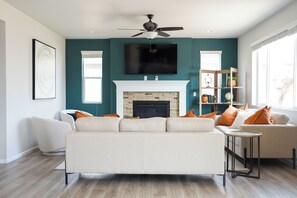 A living room with a white sofa, a fireplace, a television mounted above it, and a bookshelf. - Lovely 4-bedroom house in Bright and Charming Brighton Next to Pool and Gym (Brighton)