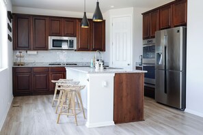 Une cuisine moderne avec des meubles en bois foncé, des appareils en acier inoxydable, un îlot central blanc doté de tabourets et un éclairage suspendu.